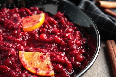 Photo of Tasty cranberry sauce with citrus fruit slices in pan on table, closeup