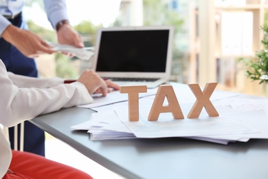 Photo of Word TAX and blurred accountants on background