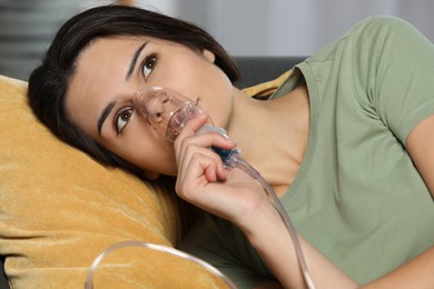 Photo of Sick young woman using nebulizer on couch at home