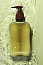 Photo of Bottle of facial cleanser in water against olive background, top view