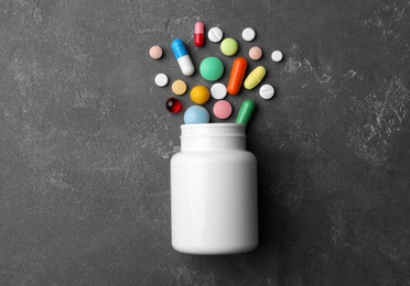 Bottle with different pills on grey background, flat lay