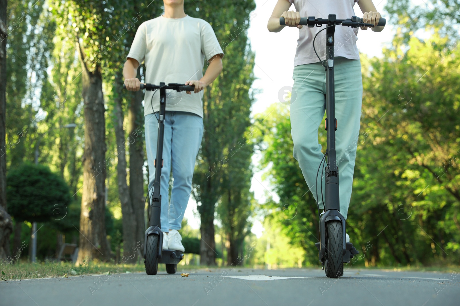 Photo of Couple riding modern electric kick scooters in park, closeup