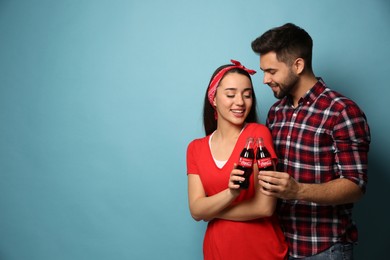 Photo of MYKOLAIV, UKRAINE - JANUARY 27, 2021: Young couple holding bottles of Coca-Cola on light blue background. Space for text