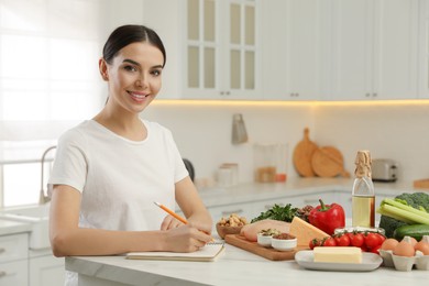 Photo of Happy woman writing in notebook near products at table. Keto diet