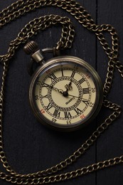 Photo of Pocket clock with chain on black wooden table, top view