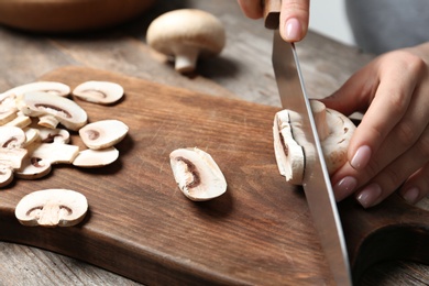 Photo of Young woman cutting fresh champignon mushrooms on wooden board, closeup view