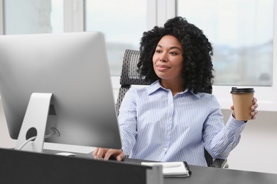 Photo of Young woman with cup of drink working on computer at table in office