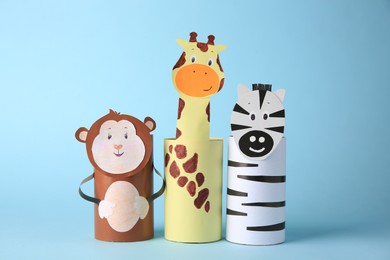 Photo of Toy monkey, giraffe and zebra made from toilet paper hubs on light blue background. Children's handmade ideas
