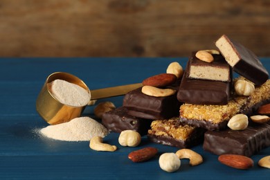 Photo of Different tasty bars, nuts and scoop of protein powder on blue wooden table