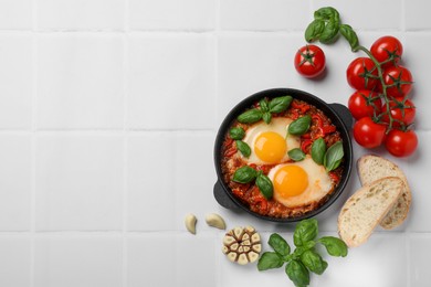 Photo of Delicious Shakshuka served on white tiled table, flat lay. Space for text