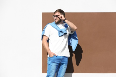 Photo of Young hipster man in stylish jeans posing near color wall