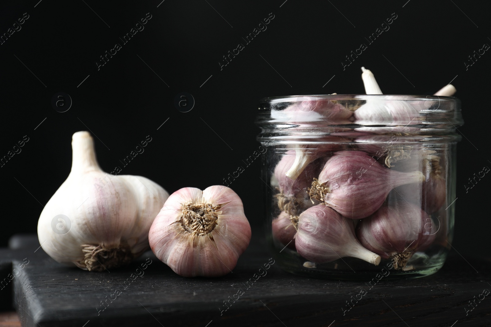 Photo of Many fresh garlic bulbs on black board, closeup