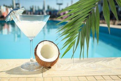 Image of View of beautiful green tropical leaves and tasty refreshing cocktail with coconut on edge of swimming pool