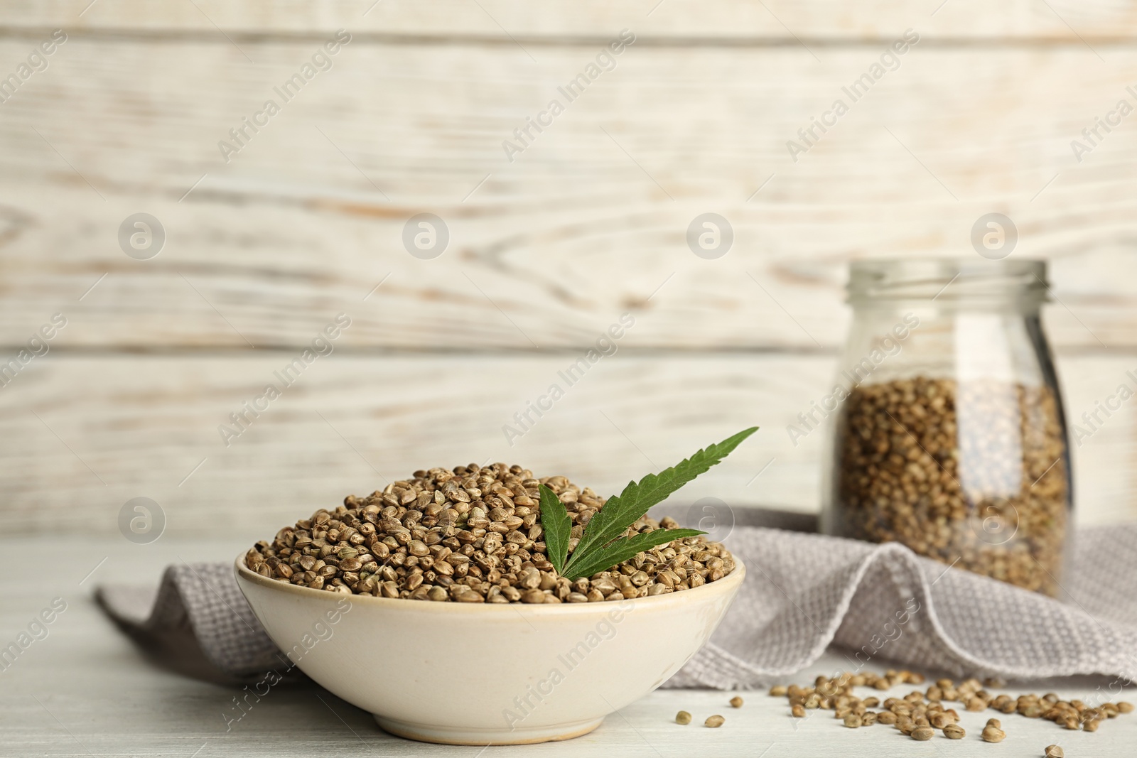 Photo of Bowl of hemp seeds on table against wooden wall