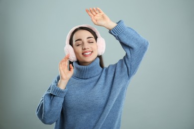 Photo of Beautiful young woman wearing earmuffs on light grey background