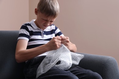 Photo of Angry boy popping bubble wrap indoors. Stress relief