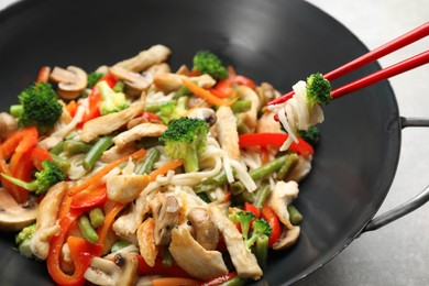 Chopsticks with stir fried noodles over wok on table, closeup