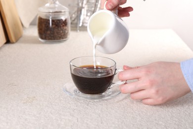 Woman pouring milk into cup with aromatic coffee at light textured table, closeup