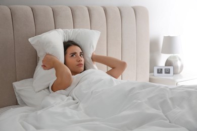 Photo of Unhappy young woman covering ears with pillow in bed at home. Noisy neighbours