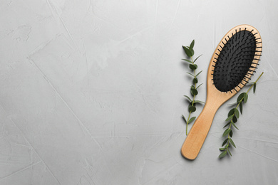 Photo of Hair brush and green twigs on light grey stone background, flat lay. Space for text
