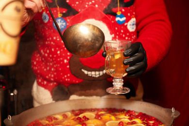 Photo of Seller pouring tasty mulled wine into cup at winter fair, closeup