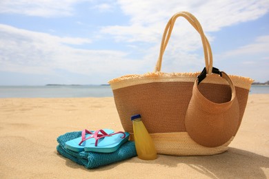 Photo of Beach accessories and bottle of refreshing drink on sand near sea, space for text