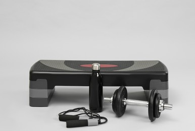 Step platform, skipping rope, dumbbell and water bottle on light background, space for text. Sport equipment