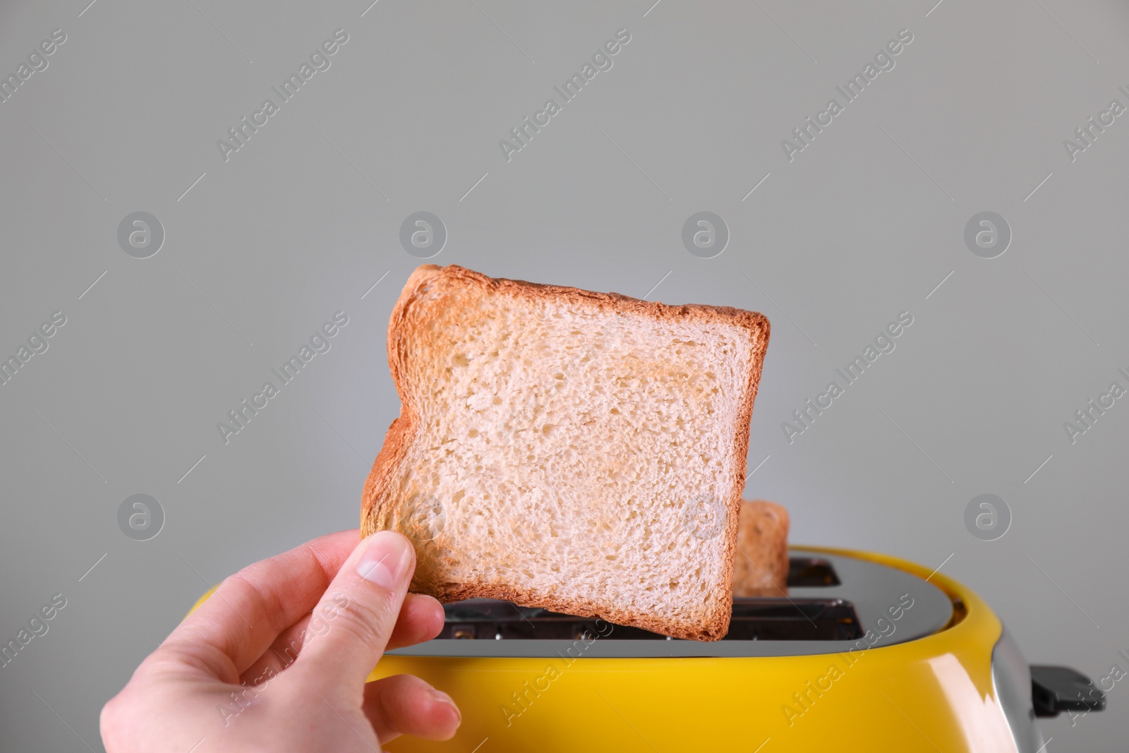 Woman taking off roasted bread from toaster against grey background, closeup Photo of Woman taking off roasted bread from toaster against grey background, closeup