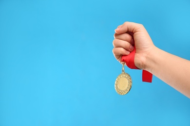 Photo of Woman holding gold medal on light blue background, closeup. Space for text