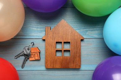 Photo of House model, keys, trinket and balloons on light blue wooden table, flat lay. Housewarming party
