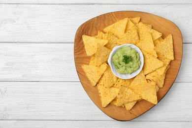 Photo of Plate with tasty Mexican nachos chips and guacamole sauce on white wooden table, top view. Space for text