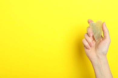 Photo of Woman with jade gua sha tool on yellow background, closeup. Space for text