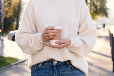 Photo of Woman holding takeaway cardboard cup on city street, closeup. Coffee to go