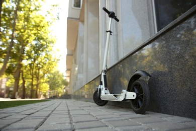 Photo of Modern electric kick scooter parked near building. Space for text