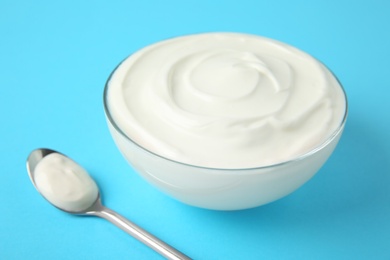 Photo of Glass bowl of sour cream and spoon on light blue background