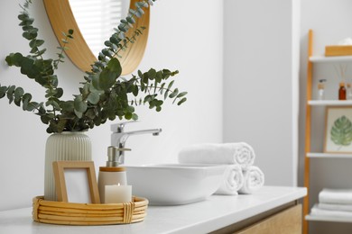 Vase with eucalyptus branches and toiletries near vessel sink in bathroom, space for text. Interior design