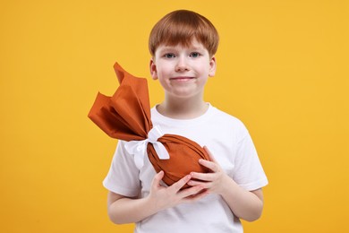 Photo of Easter celebration. Cute little boy with wrapped egg on orange background