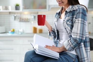 Photo of Young woman with cup of coffee reading book at home, closeup. Space for text