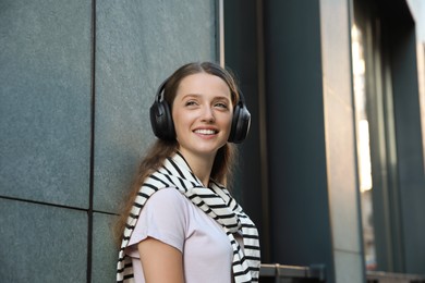 Photo of Smiling woman in headphones listening to music near building outdoors