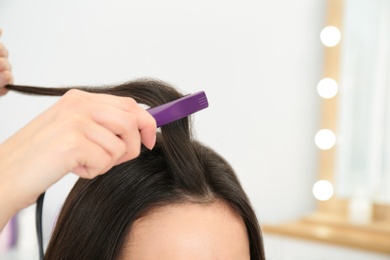 Hairdresser using modern flat iron to style client's hair in salon, closeup. Space for text