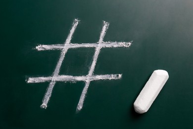 Photo of White piece of chalk and hashtag symbol drawn on blackboard, top view