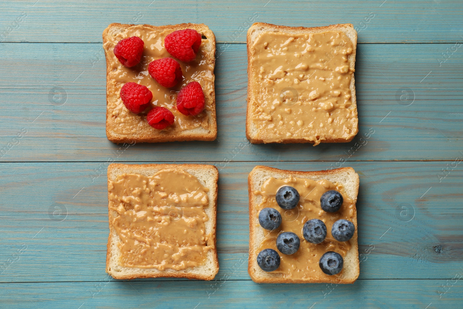 Photo of Delicious toasts with peanut butter, raspberries and blueberries on light blue wooden table, flat lay