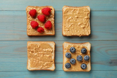 Photo of Delicious toasts with peanut butter, raspberries and blueberries on light blue wooden table, flat lay