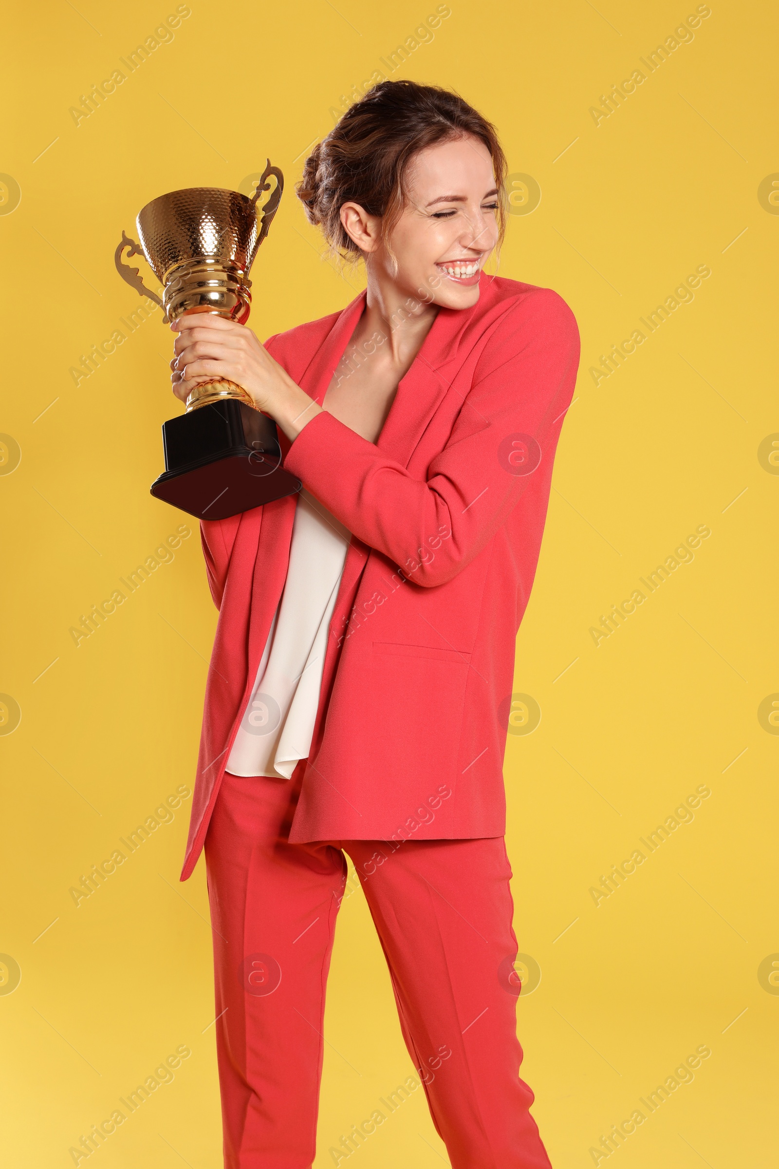 Photo of Portrait of happy young businesswoman with gold trophy cup on yellow background