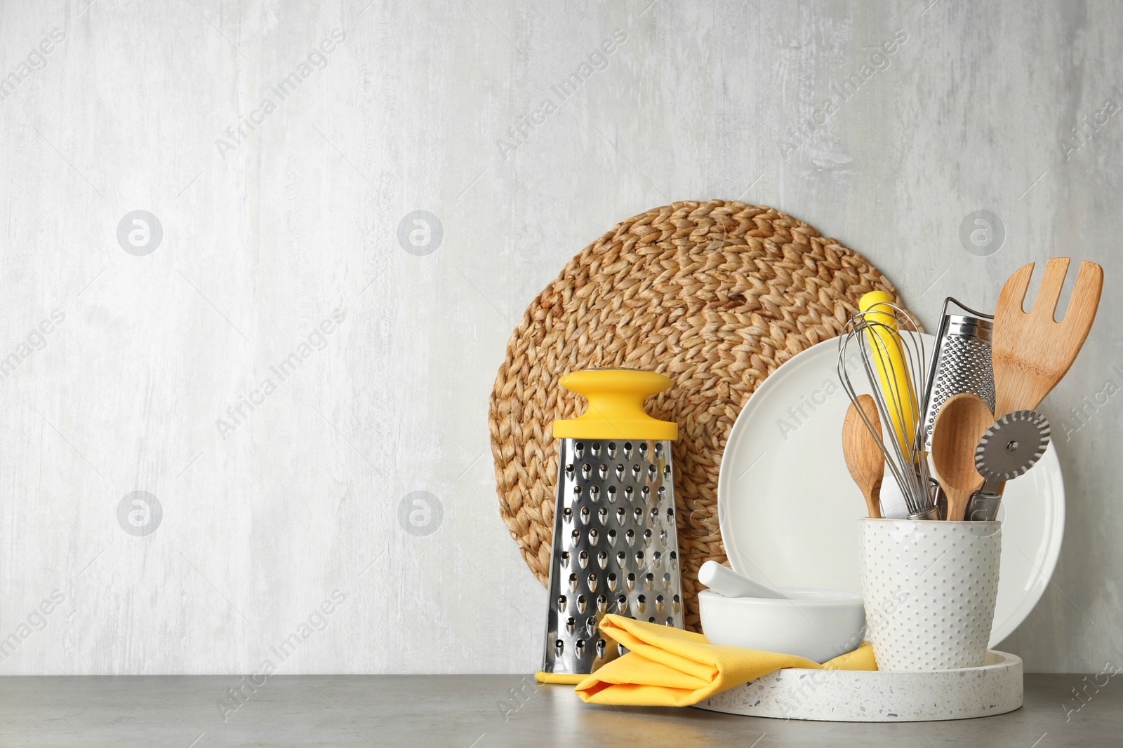 Photo of Different kitchen utensils on grey table against light background. Space for text