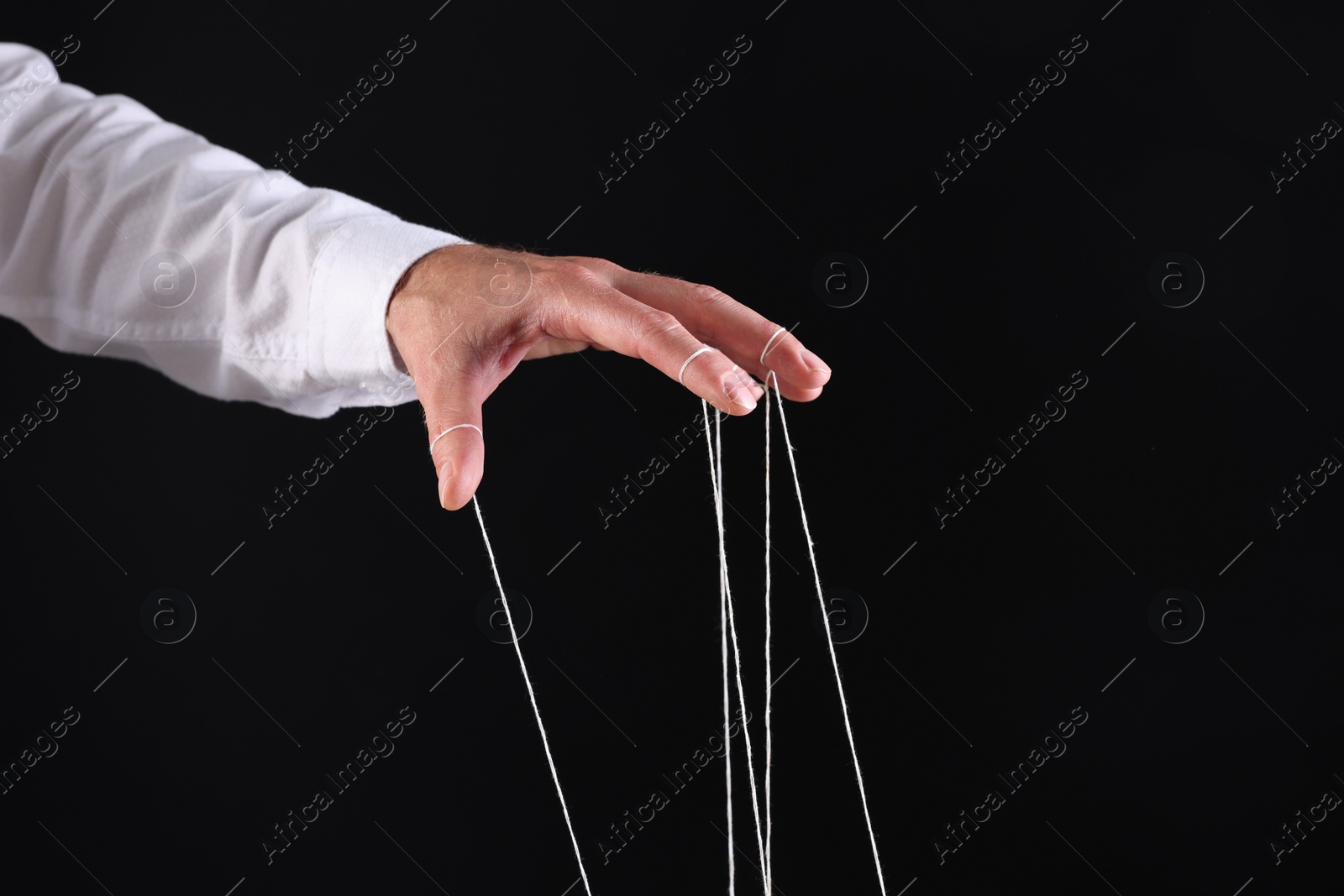 Photo of Man pulling strings of puppet on black background, closeup. Space for text