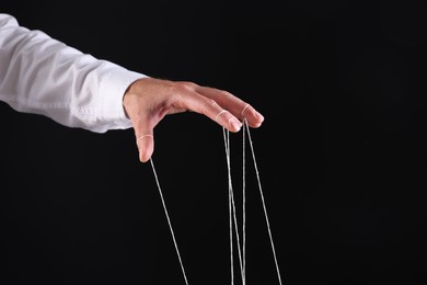 Man pulling strings of puppet on black background, closeup. Space for text