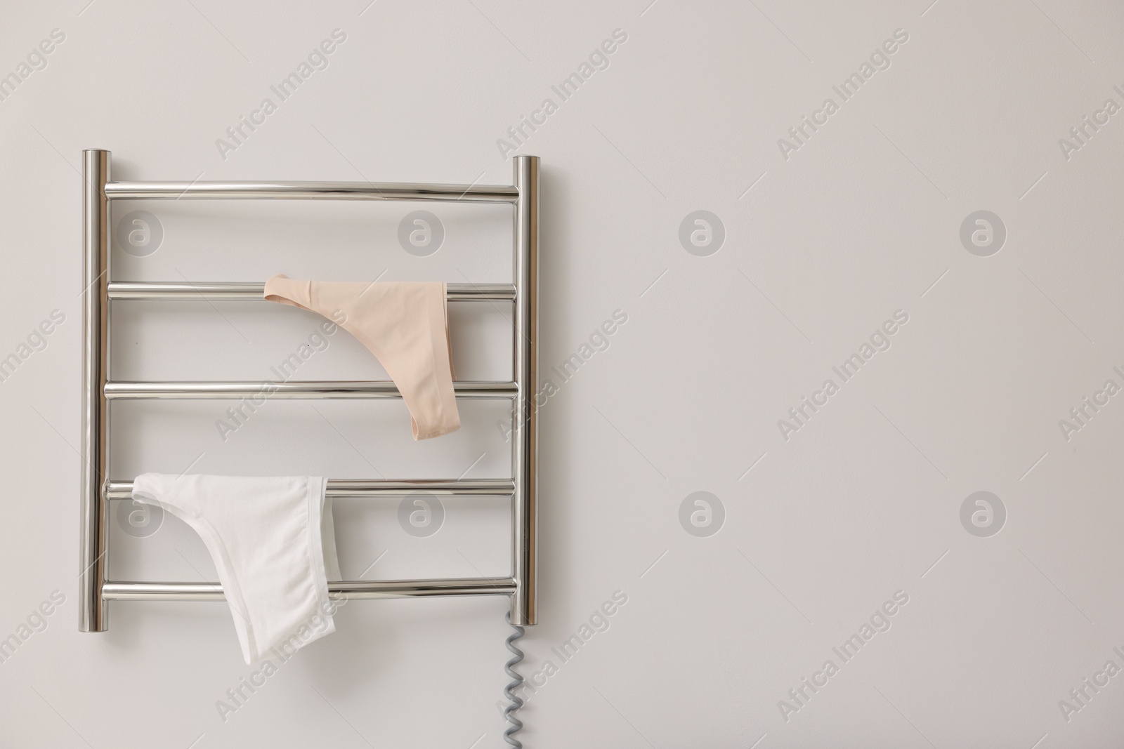 Photo of Heated towel rail with underwear on white wall, space for text