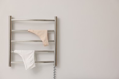 Photo of Heated towel rail with underwear on white wall, space for text