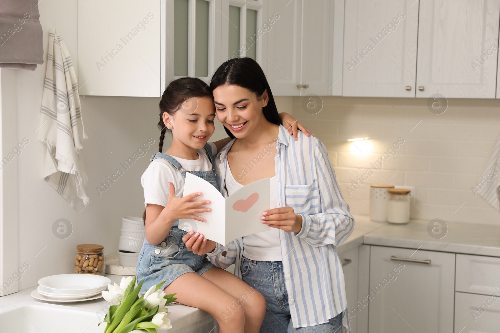 Photo of Little daughter congratulating her mom in kitchen at home. Happy Mother's Day